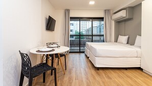 A compact hotel room with a bed, a dining table with chairs, a TV mounted on the wall, and a balcony with a view of the city. - Aurora Paulistana by Viva - Prédio completo a passos do Metrô República (São Paulo)
