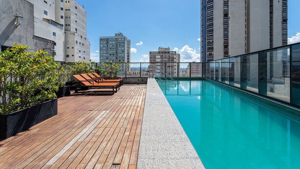 A rooftop pool with wooden deck and lounge chairs, surrounded by high-rise buildings. - Aurora Paulistana by Viva - Prédio completo a passos do Metrô República (São Paulo)