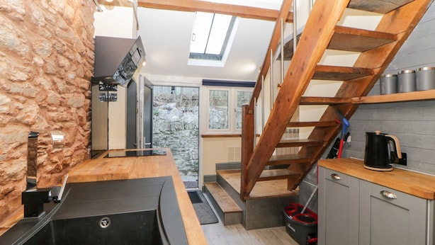 A compact kitchen with a stone accent wall, a wooden staircase, and a skylight. - Eventide (Plymouth)
