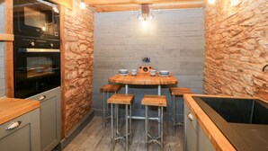 A compact kitchen with a wooden table, stools, and a built-in oven. - Eventide (Plymouth)