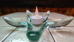 A glass candle holder with a lit candle on a tiled floor. - Your Nomadic Room : Outremer (Marthod)