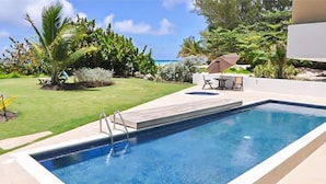 A rectangular swimming pool with a ladder, surrounded by a concrete deck, with a patio area and outdoor furniture. - 501 Ocean front condo at Ocean One Maxwell coast road Barbados (Oistins)