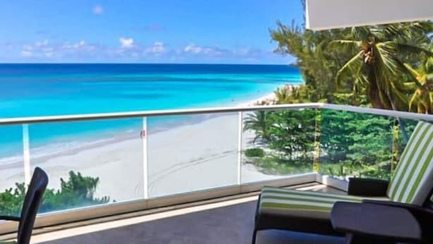 A balcony with a view of a beach and palm trees. - 501 Ocean front condo at Ocean One Maxwell coast road Barbados (Oistins)