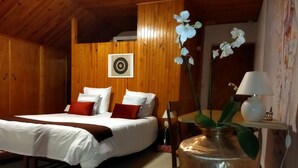 A bedroom with a bed, pillows, a bedside table with a lamp, a vase with flowers, and a wall-mounted picture.