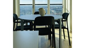 Ein Essbereich mit Tisch und Stühlen, eine Vase auf dem Tisch und ein Blick auf die Stadt durch große Fenster.