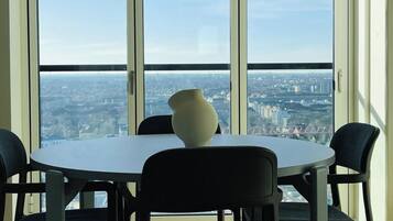 A dining area with a table and chairs, a vase on the table, and a city view through large windows.