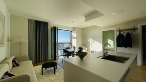 Ein modernes Hotelzimmer mit Essbereich, einem großen Fenster mit Blick auf die Stadt, einer Couch und einem kleinen Hund.