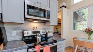 A modern kitchen with stainless steel appliances, a wooden dining table, and a view of the outdoors.