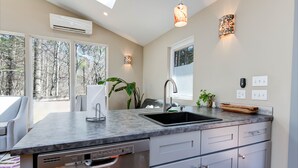 A modern kitchen with a large island, built-in dishwasher, and a window overlooking a forest.