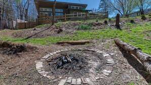 A rustic outdoor area with a fire pit, wooden fence, and a building in the background.