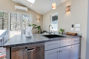 Una cocina moderna con una isla grande, lavavajillas integrado y ventana con vistas a un bosque.