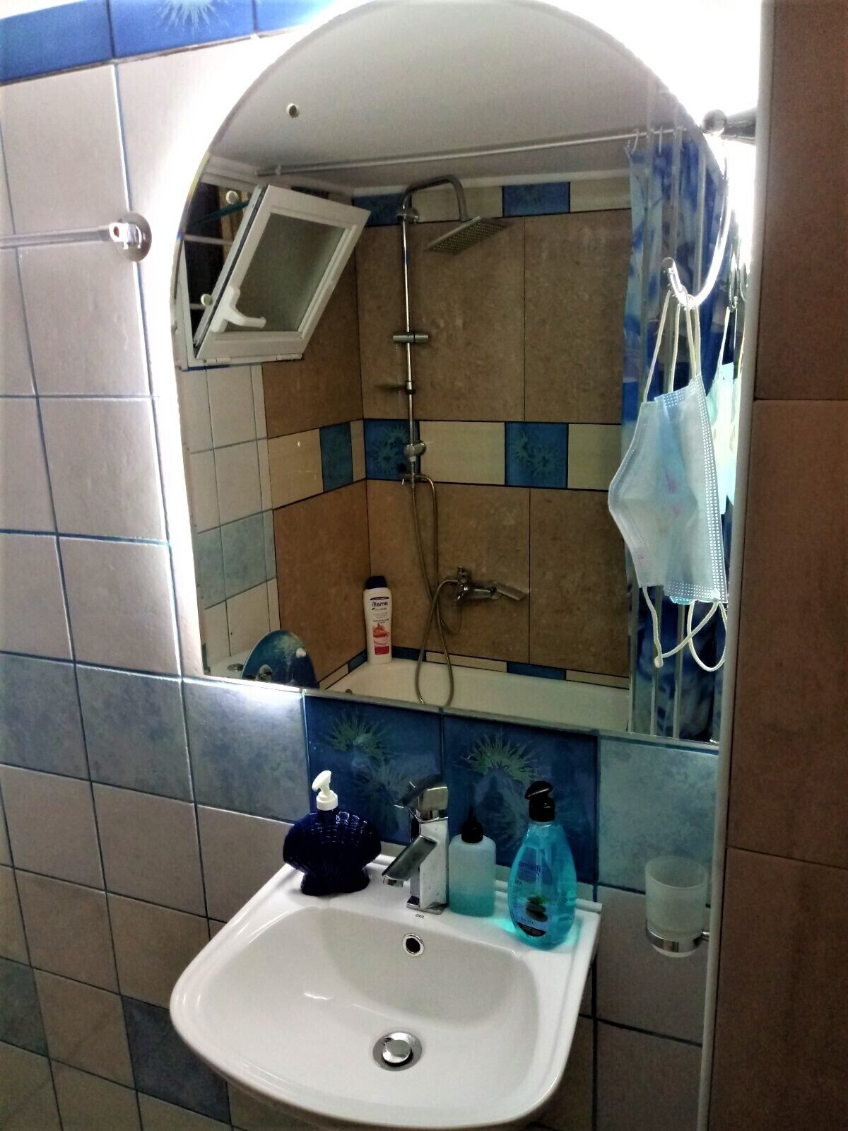 Casa de banho com lavatório, espelho, chuveiro e paredes em azulejo.
