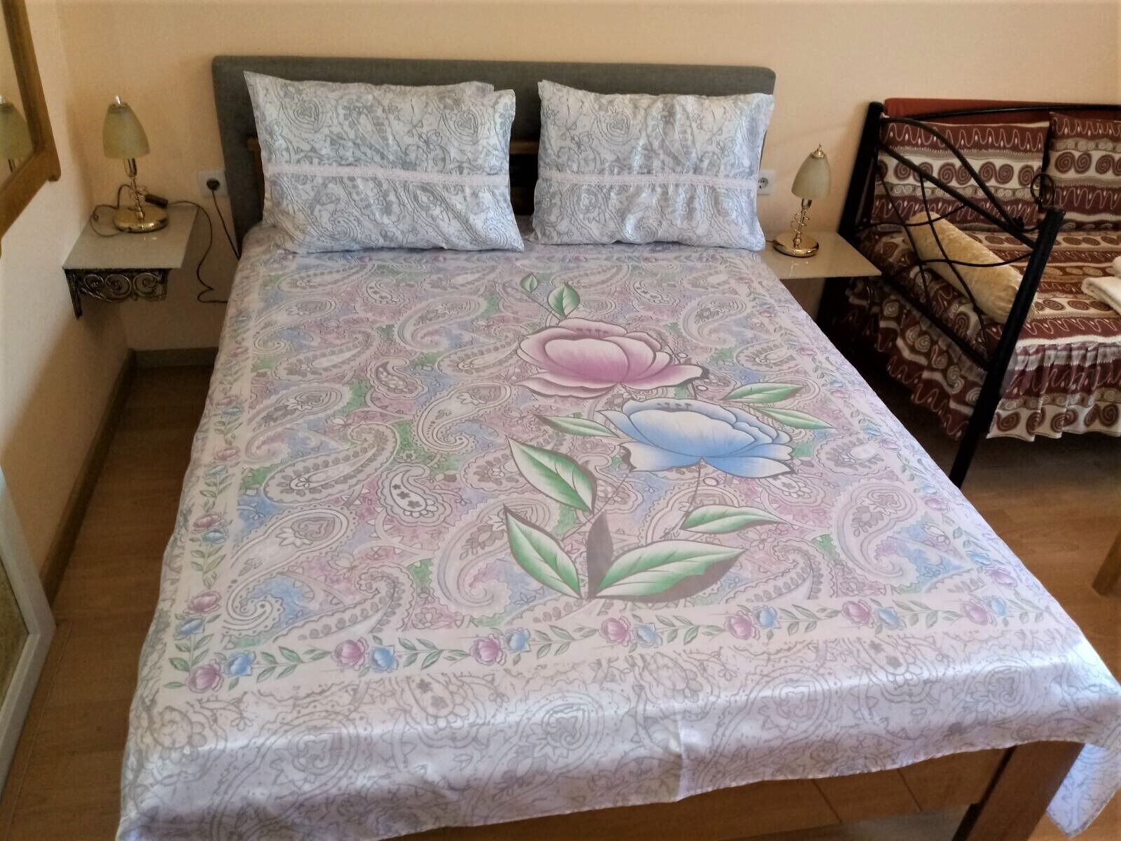Una cama con una colcha de motivos florales, dos almohadas y dos lámparas de noche.