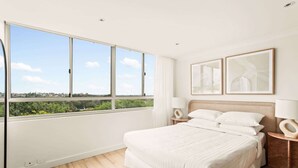 A bedroom with a large window, a bed, two bedside tables with lamps, and two framed pictures on the wall.