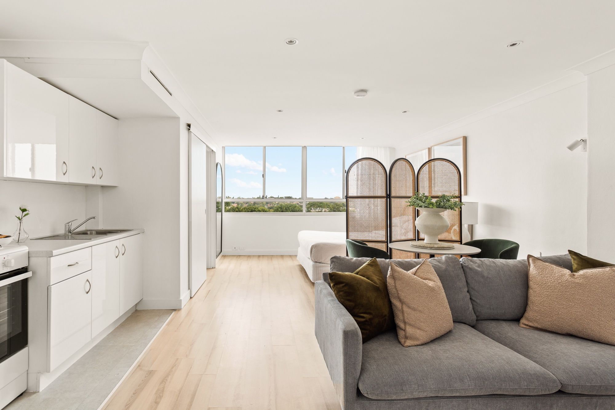 A modern kitchen with white cabinets, a built-in oven, and a window overlooking a landscape.