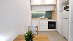 A compact kitchen with white cabinets, a green-tiled backsplash, a built-in oven, and a microwave. - Charming Loft in the Historic Center of Manresa. (Manresa)
