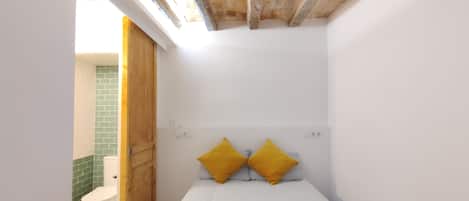 Een kleine, compacte kamer met een bed, een houten deur en een wand betegeld met groene tegels.
