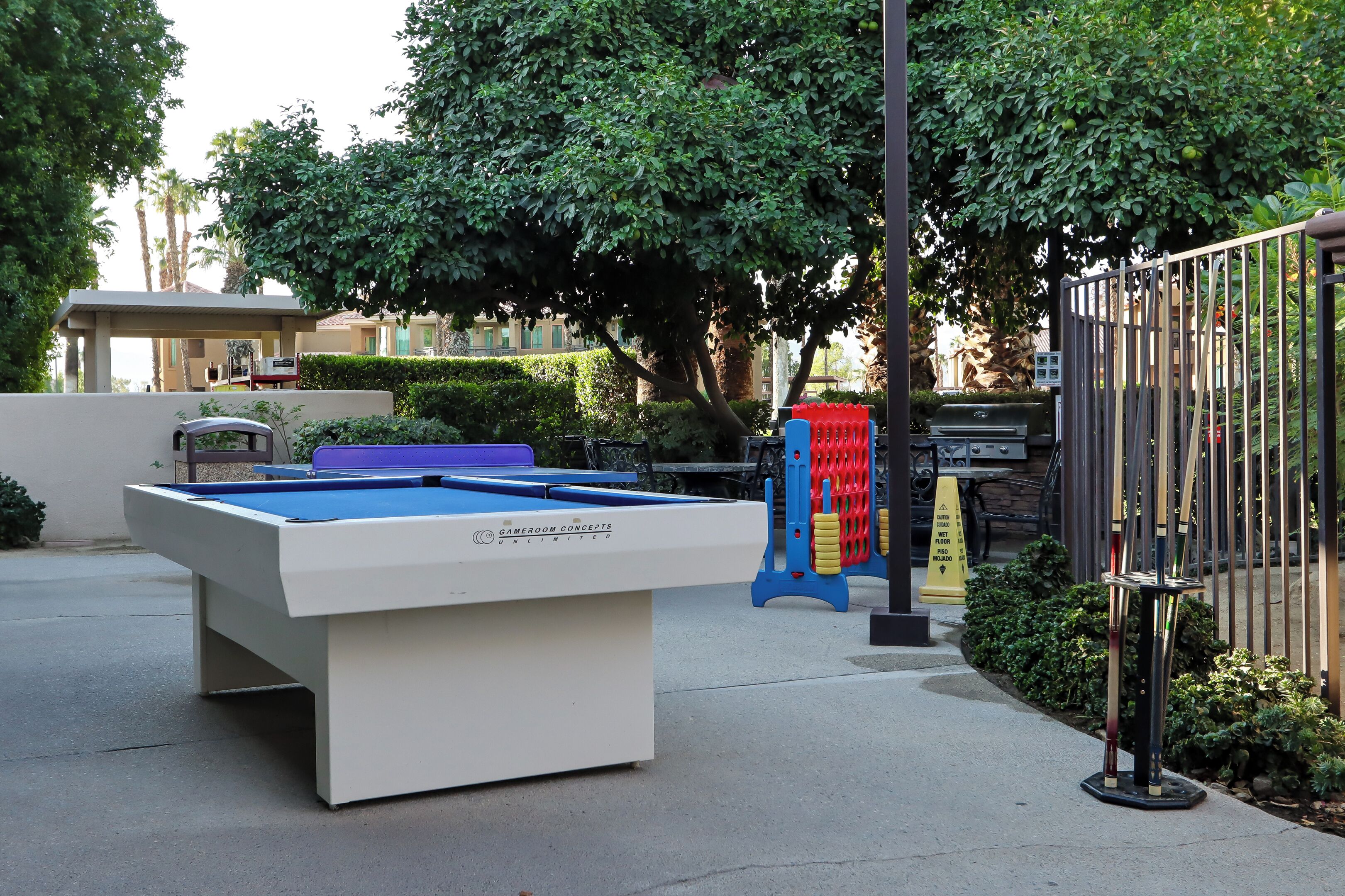 A pool table in an outdoor setting with a fence and greenery in the background.