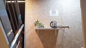 A staircase with a metal railing leading to a landing. On the landing, there is a wall-mounted shelf with a plant and a kettle. A 'No Smoking' sign is visible on the wall. - Foresttel Bkk - Hostel (Bangkok)