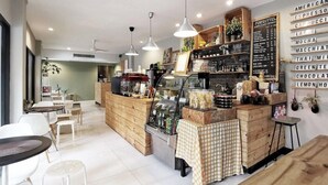A café with a wooden counter, a menu board, and seating areas with tables and chairs. - Foresttel Bkk - Hostel (Bangkok)