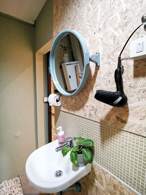 A bathroom with a white sink, a mirror, a hairdryer, a potted plant, and a toilet paper roll. - Foresttel Bkk - Hostel (Bangkok)