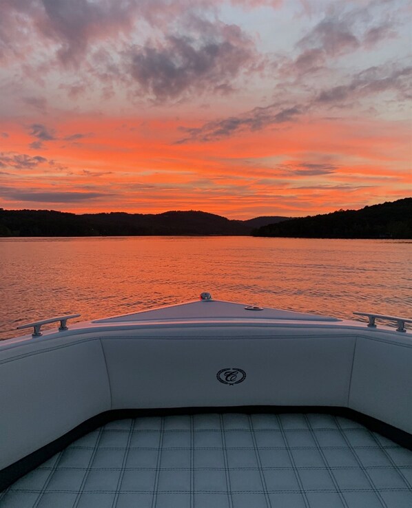 A boat's deck with a logo, a calm lake, and a sunset sky. - 4BR Poolside Retreat w/ Hot Tub + Boat Slip (Branson)