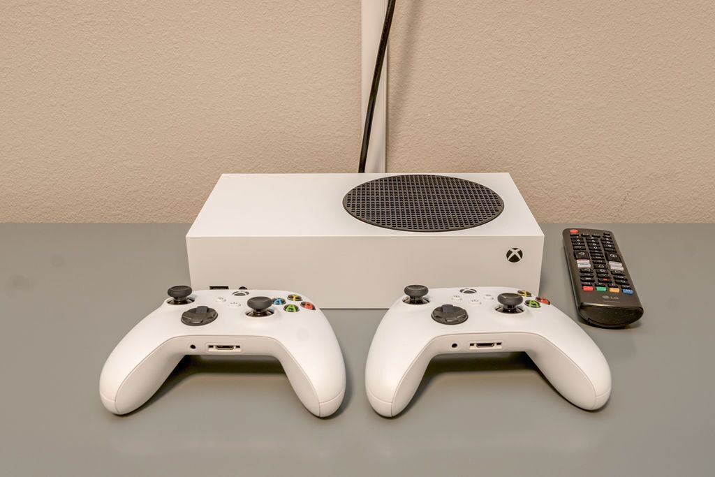 A white Xbox console with two controllers and a remote on a grey surface.