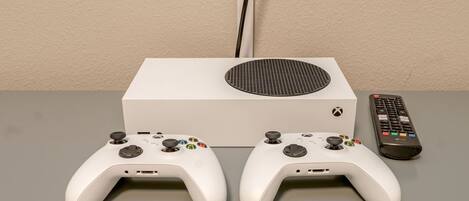 A white Xbox console with two controllers and a remote on a grey surface.