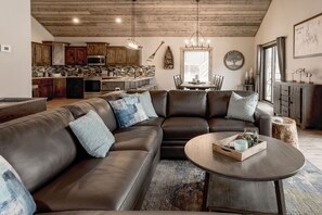 A spacious living area with a large leather sectional sofa, a round coffee table, and a kitchen in the background. - 4BR Poolside Retreat w/ Hot Tub + Boat Slip (Branson)