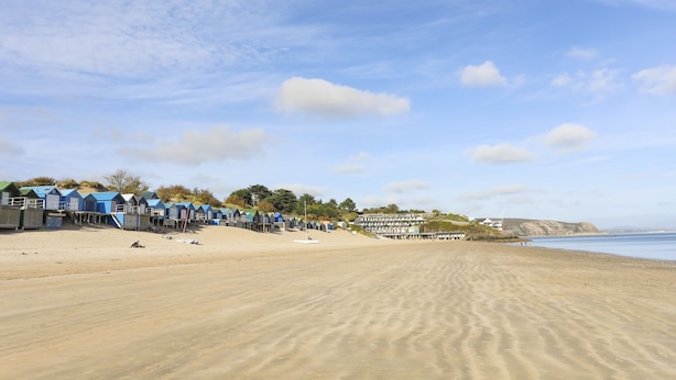 Een strand met een rij blauwe strandhutten en een zandstrand.