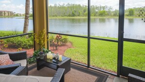 Un patio con muebles de mimbre, una mesita con velas y vistas a un lago y follaje verde.