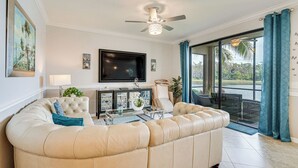 Una sala de estar con un amplio sofá seccional color beige, un televisor de pantalla plana montado en la pared y un gran ventanal con vistas al exterior.