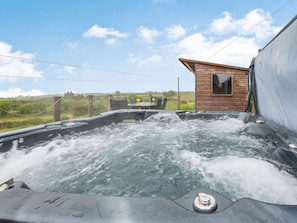 Een bubbelbad met een houten hutje op de achtergrond, omringd door een gazon en een hek.