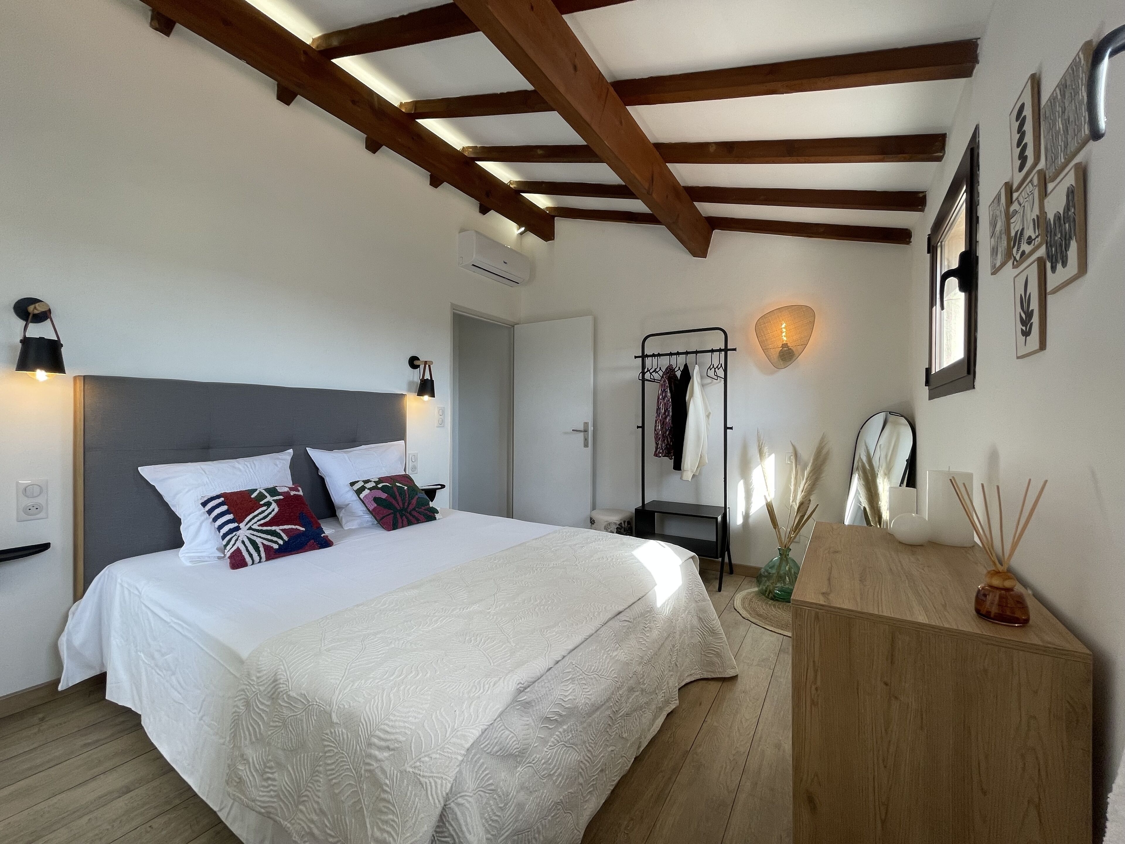 A bedroom with a bed, wooden beams, a wardrobe, a mirror, and wall art.