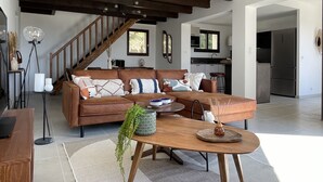 Ein modernes Wohnzimmer mit einer braunen Ledersofa, einem Holztisch und einer Treppe mit sichtbaren Holzbalken.