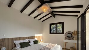 Ein Schlafzimmer mit Bett, Nachttisch, Fenster und einem dekorativen Spiegel.