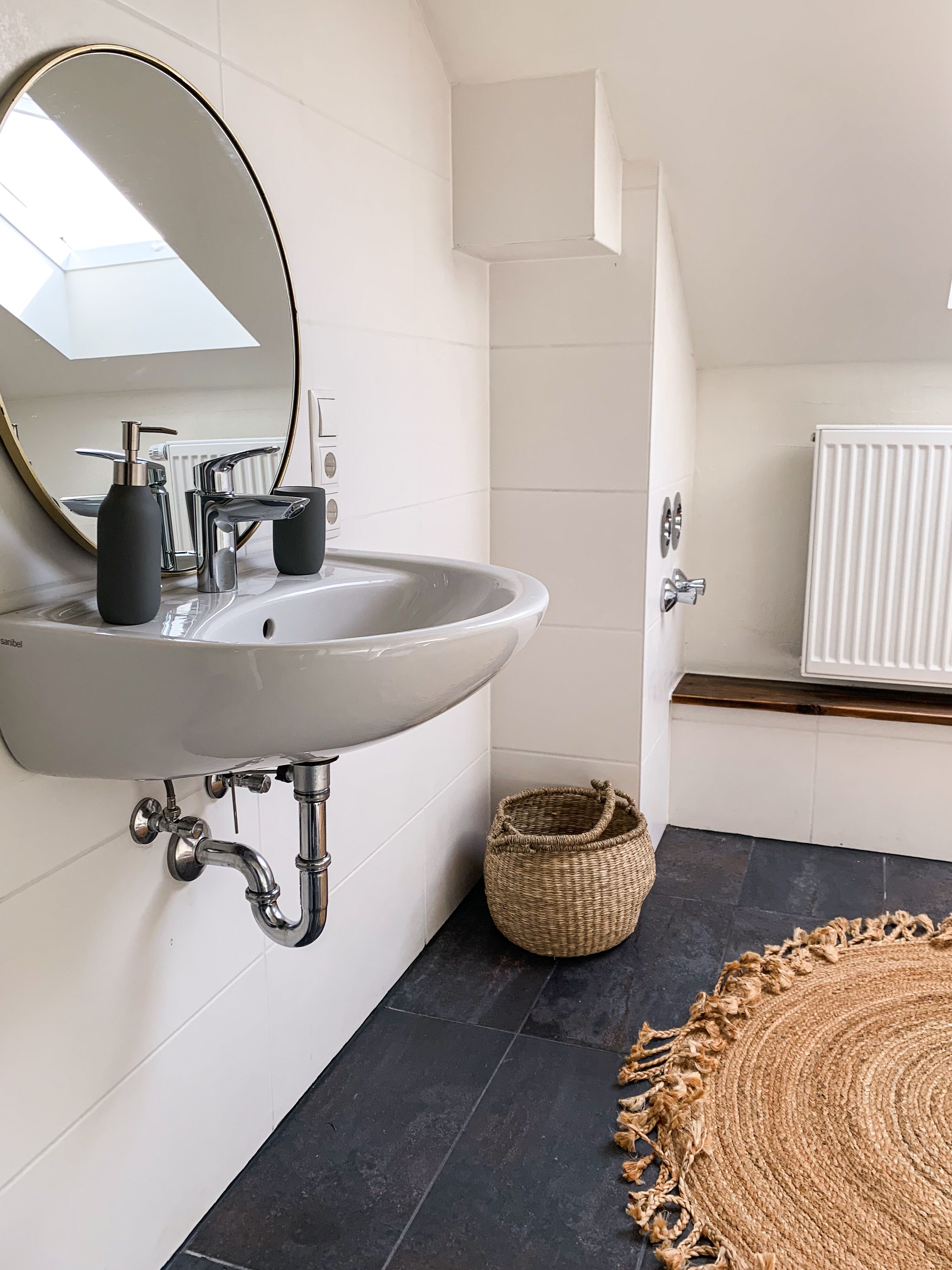 A bathroom with a white sink, a round mirror, a black floor, and a woven basket.