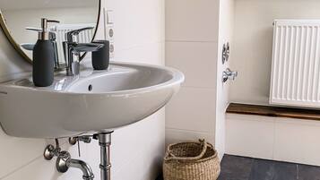 A bathroom with a white sink, a round mirror, a black floor, and a woven basket.