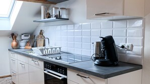 Une cuisine moderne avec des armoires blanches, un comptoir noir et un four encastré. On y trouve également une machine à café et une bouilloire sur le comptoir.
