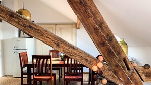 Un coin repas rustique avec des chaises et une table en bois, un réfrigérateur blanc et une structure en poutres apparentes.