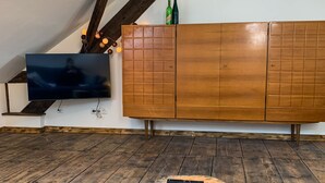 Une pièce avec un plancher en bois, un téléviseur fixé au mur et un meuble en bois sur lequel sont posées des bouteilles.