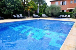 Une piscine d’un bleu éclatant, avec des chaises longues et un bâtiment en arrière-plan.