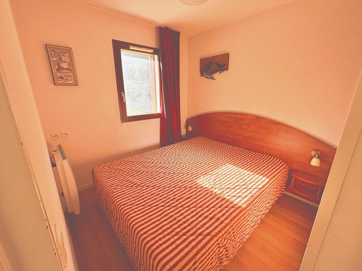 A bedroom with a bed, a window, a nightstand, and a wall-mounted artwork.