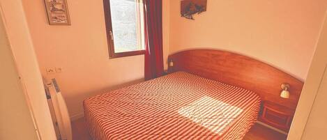 A bedroom with a bed, a window, a nightstand, and a wall-mounted artwork.