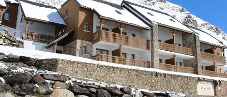 Un hotel de varios pisos con paredes de piedra y balcones de madera, con una imponente montaña nevada de fondo.