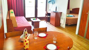 A compact hotel room with a dining table set for two, a sofa, a small desk, and a bed.