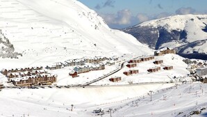 A snow-covered mountain resort with multiple chalet-style buildings, ski slopes, and a ski lift.