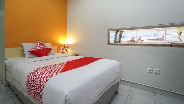 Una cama bien tendida con una colcha de lunares rojos y blancos, una almohada roja y una mesita de noche con una lámpara.