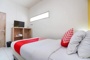 A bedroom with a bed, a TV on a wooden stand, a window, and a door. - Cityzen Renon Hotel (Denpasar)