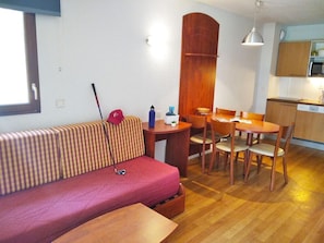 Espaço compacto para viver, com sofá, mesa de jantar, cadeiras, cozinha e janela.